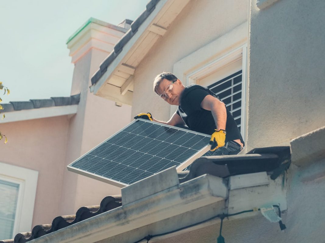A technician in protective gear installs solar panels on a house roof, promoting sustainability.